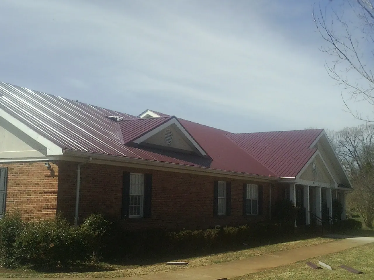 Red metal roof with gabled entries on a long brick building, from a Hail Damage Roof Repair job in Bryan