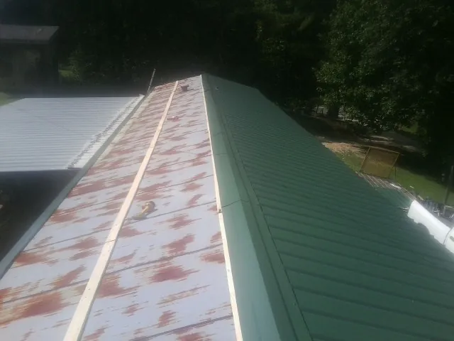 Old rusted panels beside newly installed green metal roofing — Wind Damage Roof Repair by Roofing Brothers in Bryan