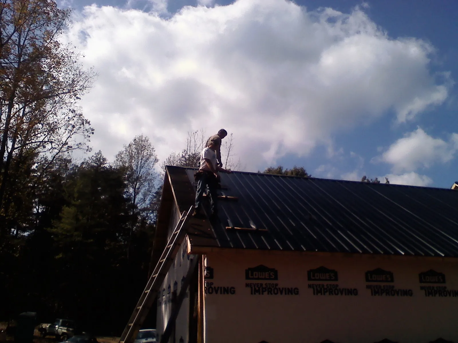 Roofer fastening dark metal panels high against a cloudy sky, from a Roof Inspection job in Bryan