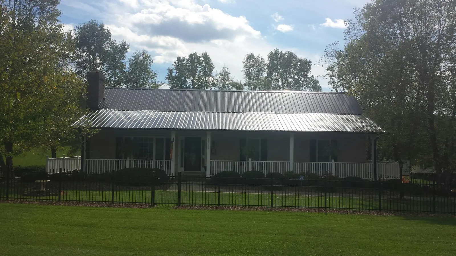 Gray metal roof on a brick ranch with a full width front porch — Gutter Guard Installation work by our crew in Bryan