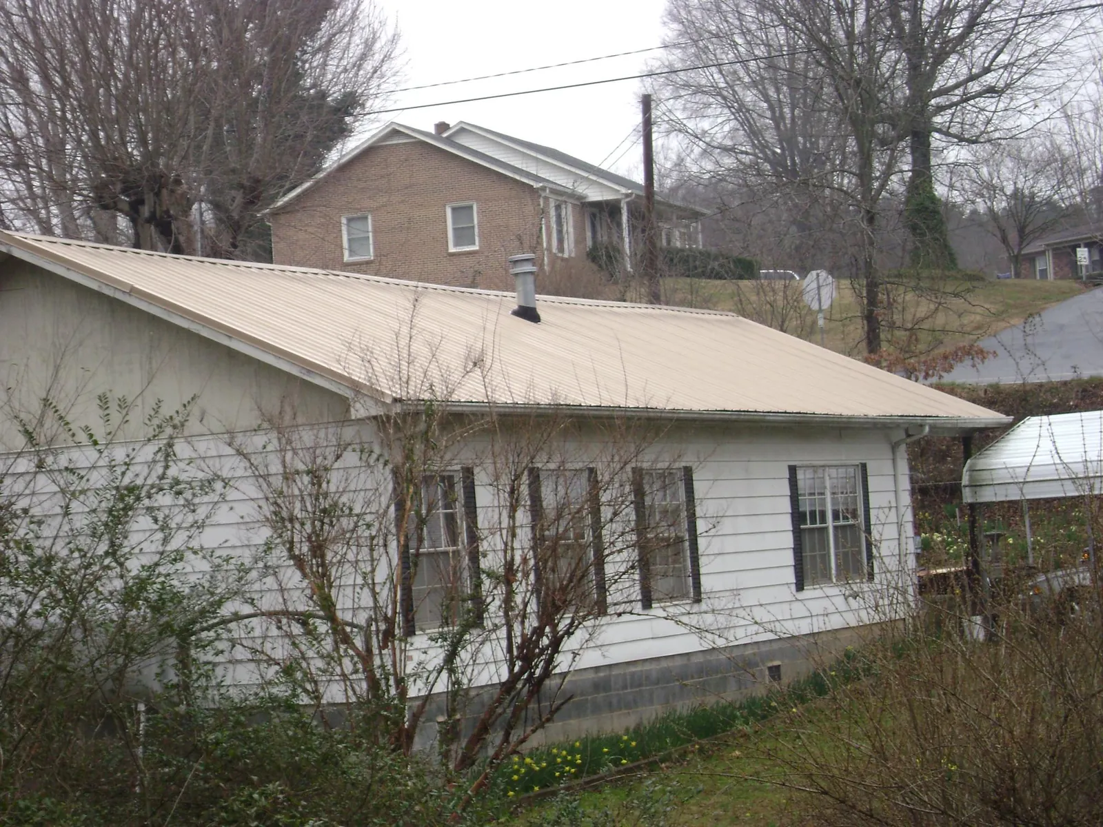 Tan metal roof on a white sided house set into a hillside — Commercial Roofing by Roofing Brothers in Bryan
