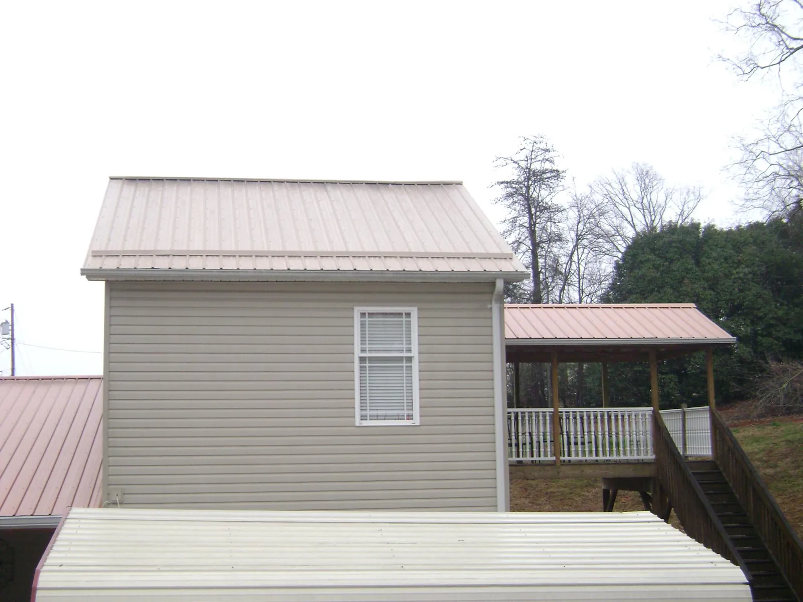 Tan metal roofs on a two story addition and attached porch, from a Roof Replacement job in Bryan