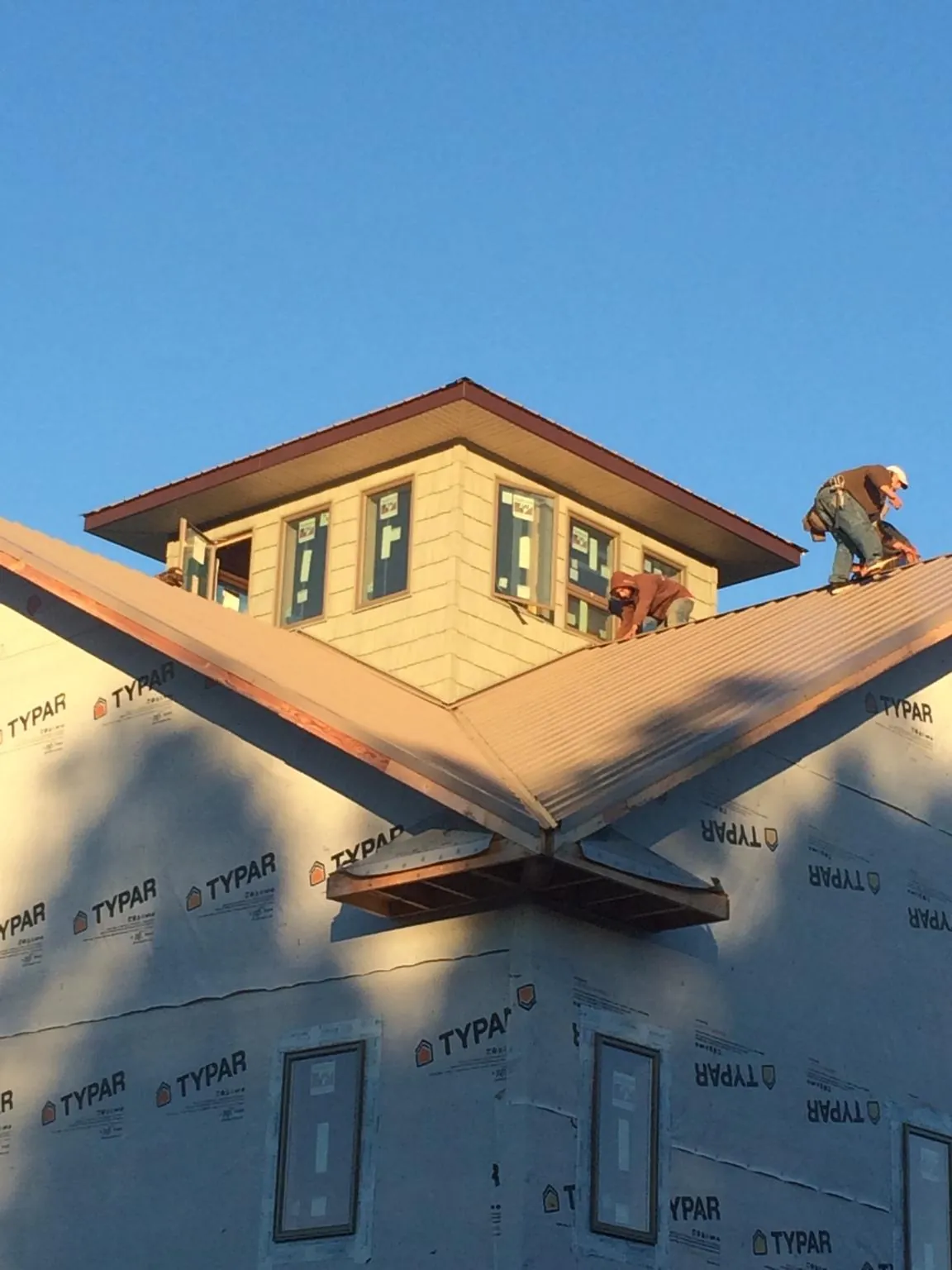 Roofers working around a rooftop cupola on a new metal roof at sunset — Roof Waterproofing in Bryan by Roofing Brothers